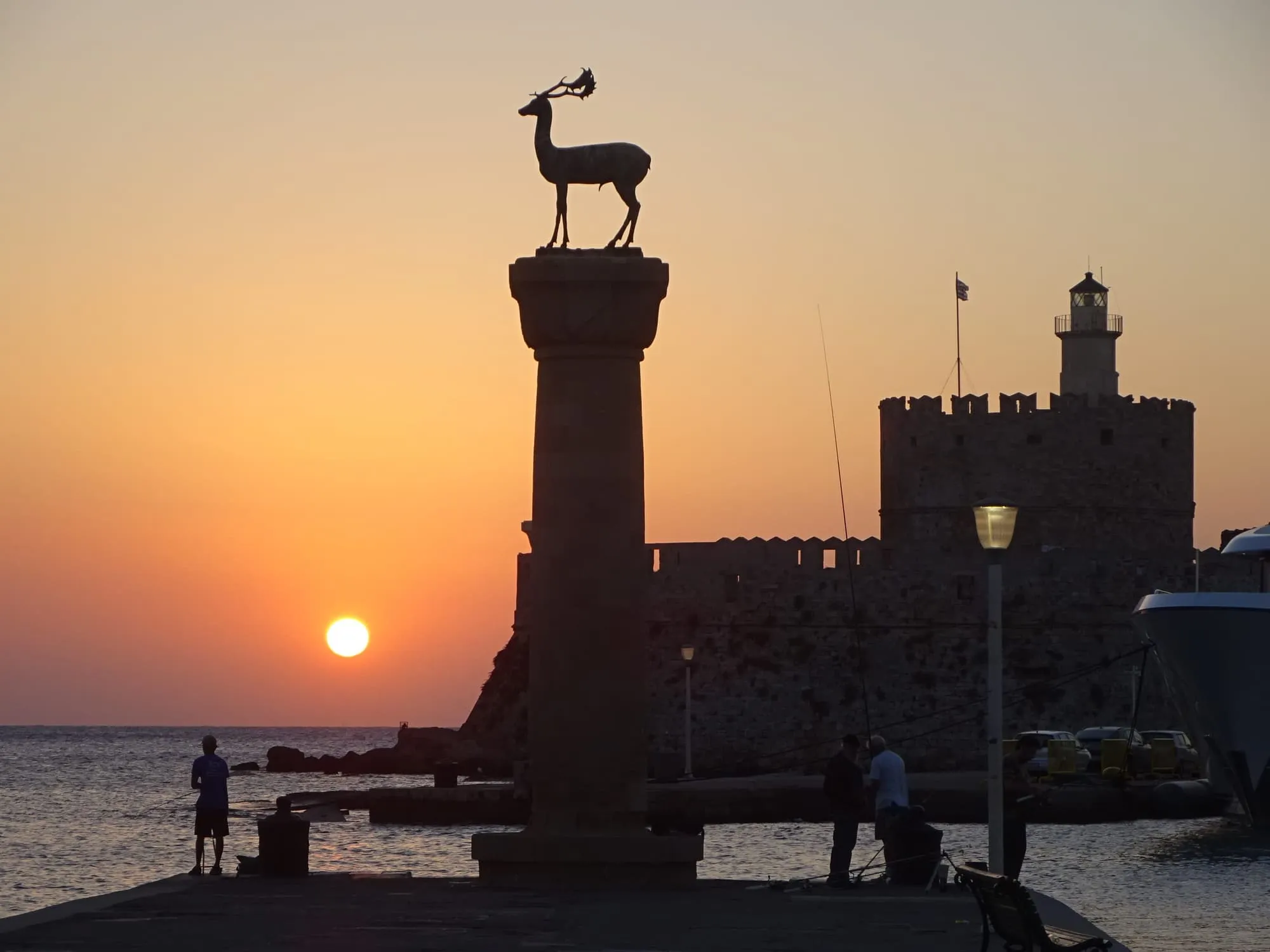 La statue du cerf sur sa colonne au port de Mandraki, avec le fort Saint-Nicolas au lever du soleil